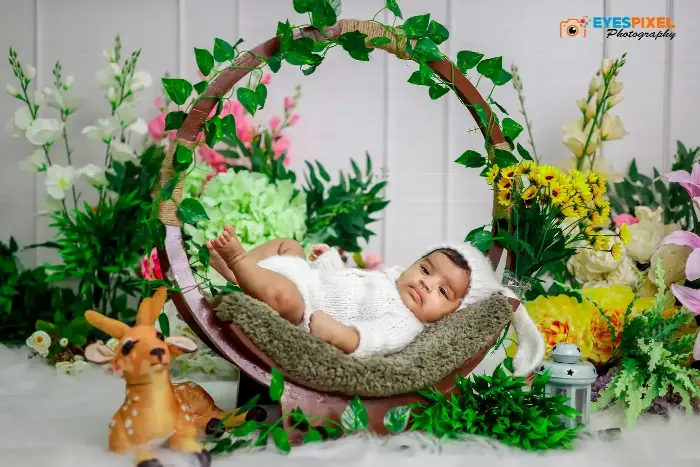 Baby resting in a round hanging prop surrounded by artificial flowers and greenery, Pune studio setup