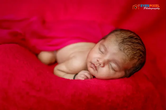 Sleeping newborn curled on a red blanket, head resting on their hands, in a warm studio in Pune