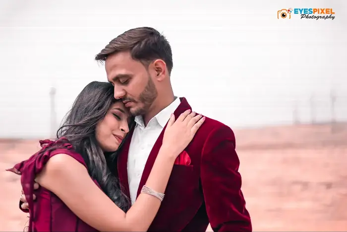 Couple in matching deep red outfits embracing, eyes closed, against a pale wall